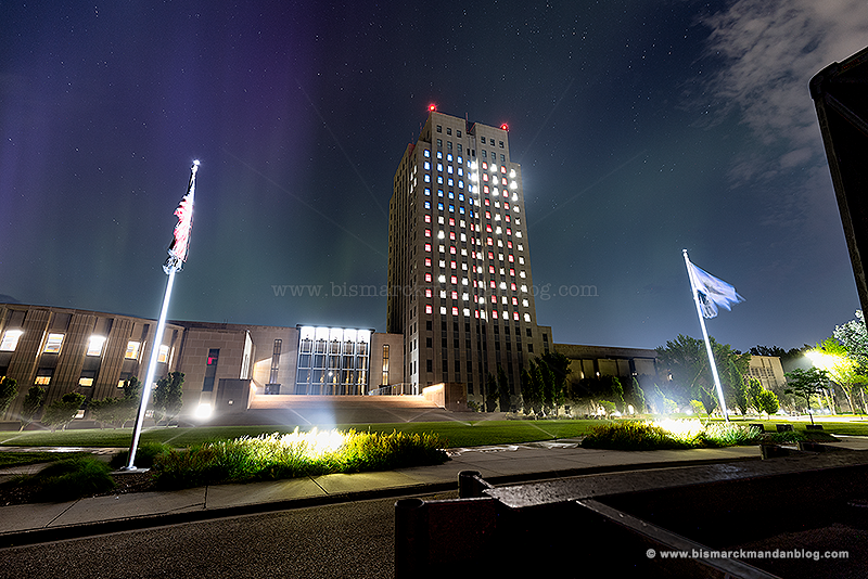 The capitol lit up with the flag colors in the windows, some northern lights in the sky, and a little bit of the Night Life stage trailer in the foreground.