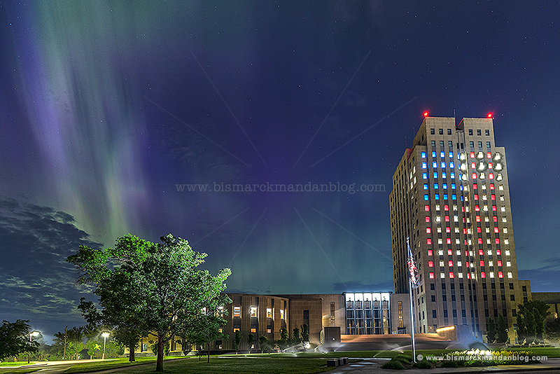 Medium angle of the capitol tower lit up with red, white, and blue windows in a flag pattern for Independence Day, with a spike of northern lights in the sky behind it
