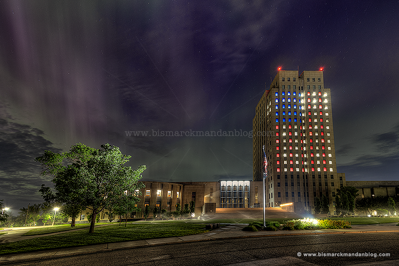 Wide angle of the capitol tower lit up with red, white, and blue windows in a flag pattern for Independence Day, with northern lights in the sky behind it